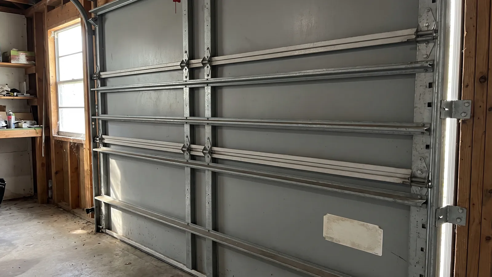 Inside of a closed impact-rated garage door showing horizontal struts, heavy hinges and jamb brackets, with the design-pressure label on an end stile